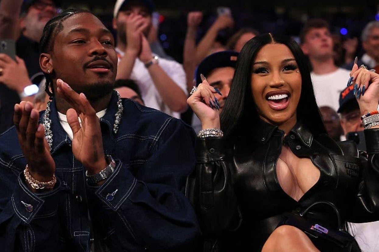 Two people sitting in a crowd at an event. The woman wears a stylish leather outfit, laughing and clapping with the man beside her