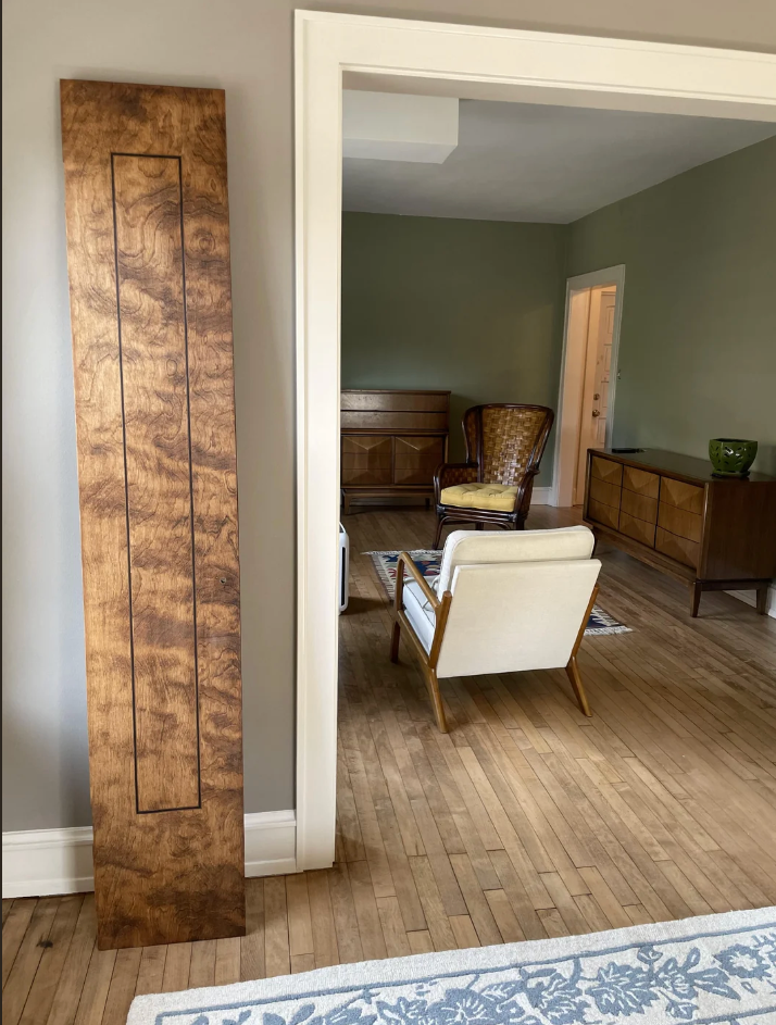 Midt århundre moderne stue med tremøbler, lett lenestol og et dekorativt trepanel som lener seg mot veggen