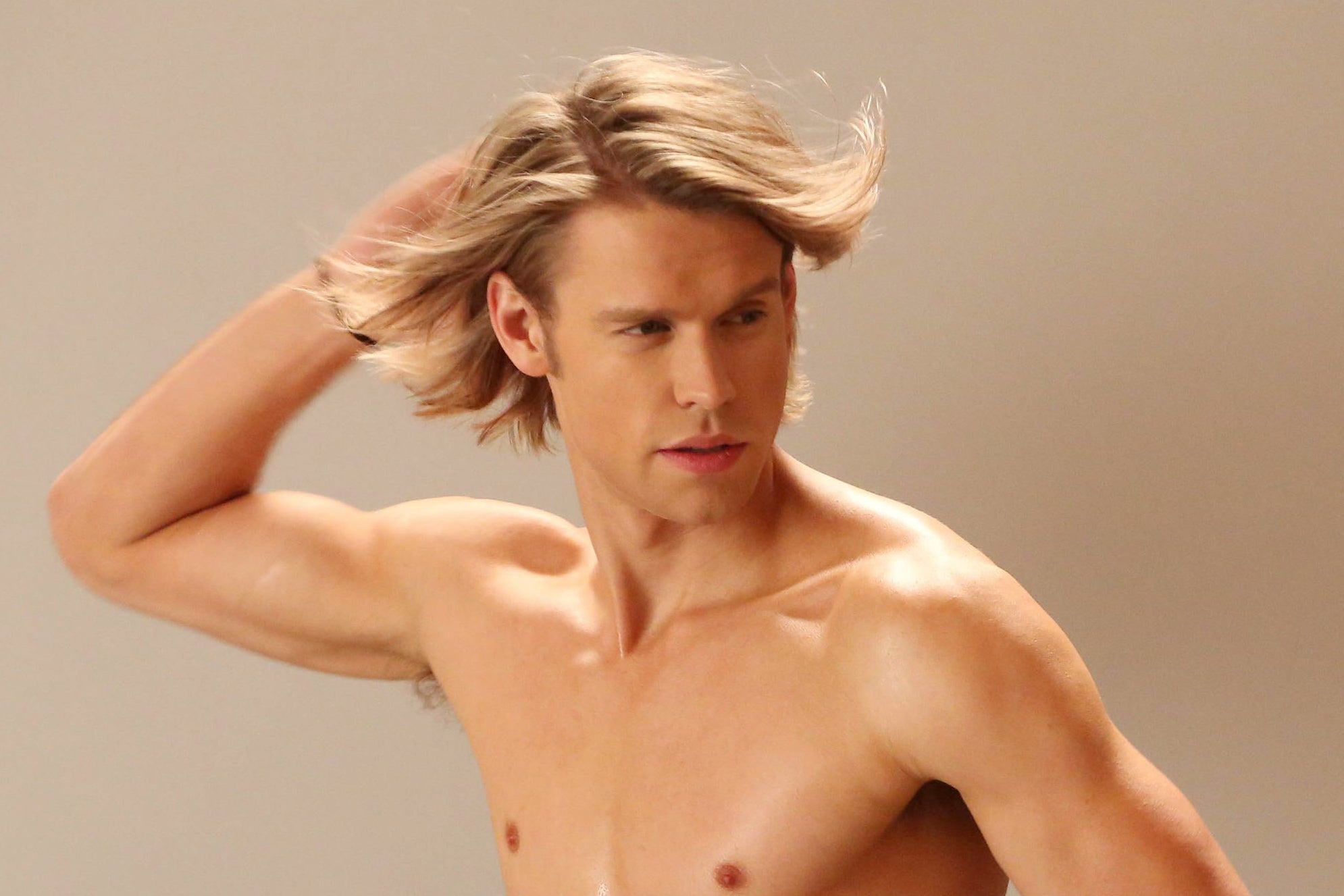 Shirtless man with toned physique poses as a woman with long hair holds a fan for a photoshoot