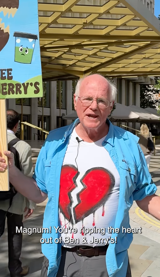 Man in casual clothing holds protest sign outside a building. Text reads: "Magnum! You're ripping the heart out of Ben &amp;amp; Jerry's!"