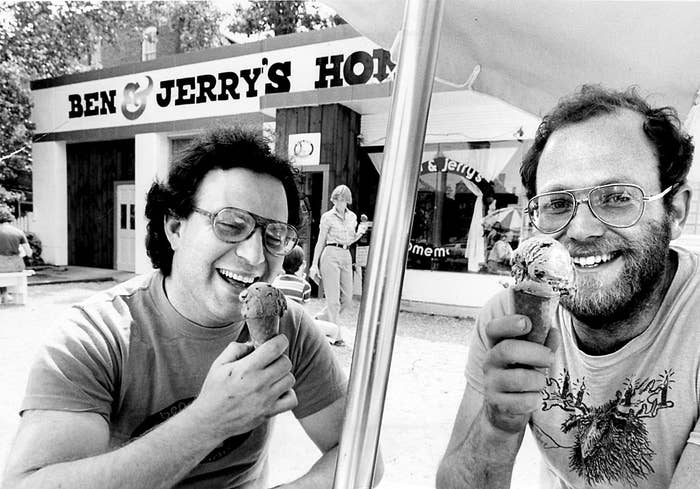 Jerry Greenfield and Ben Cohen, partners of a homemade ice cream stand, Ben &amp;amp; Jerry's, smiling while eating ice cream cones outside of Ben &amp;amp; Jerry's Vermont shop. One wears a sweater with a deer illustration