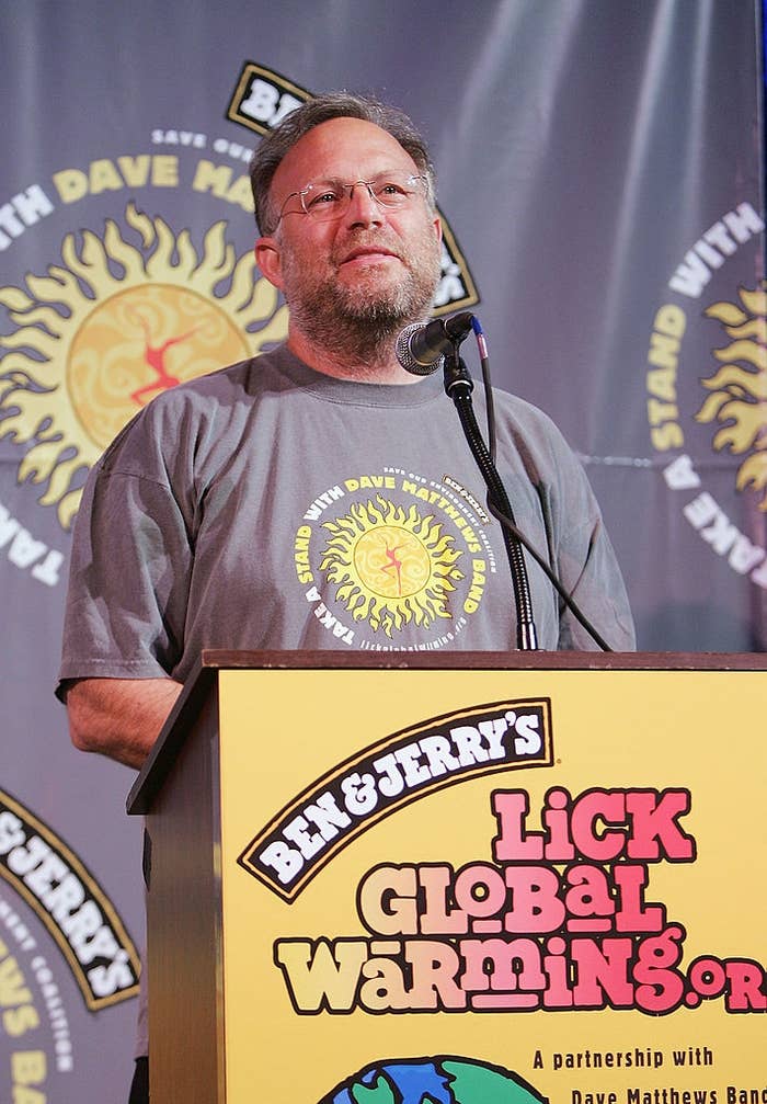A man speaks at a podium during a Ben &amp;amp; Jerry's event, promoting climate awareness, with banners featuring campaign logos in the background