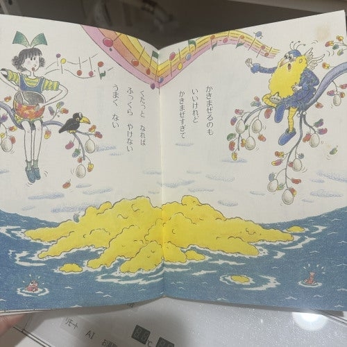 絵本のページに、浮かぶ黄色い島と枝に座るキャラクターが描かれている。日本語での文章が書かれている。