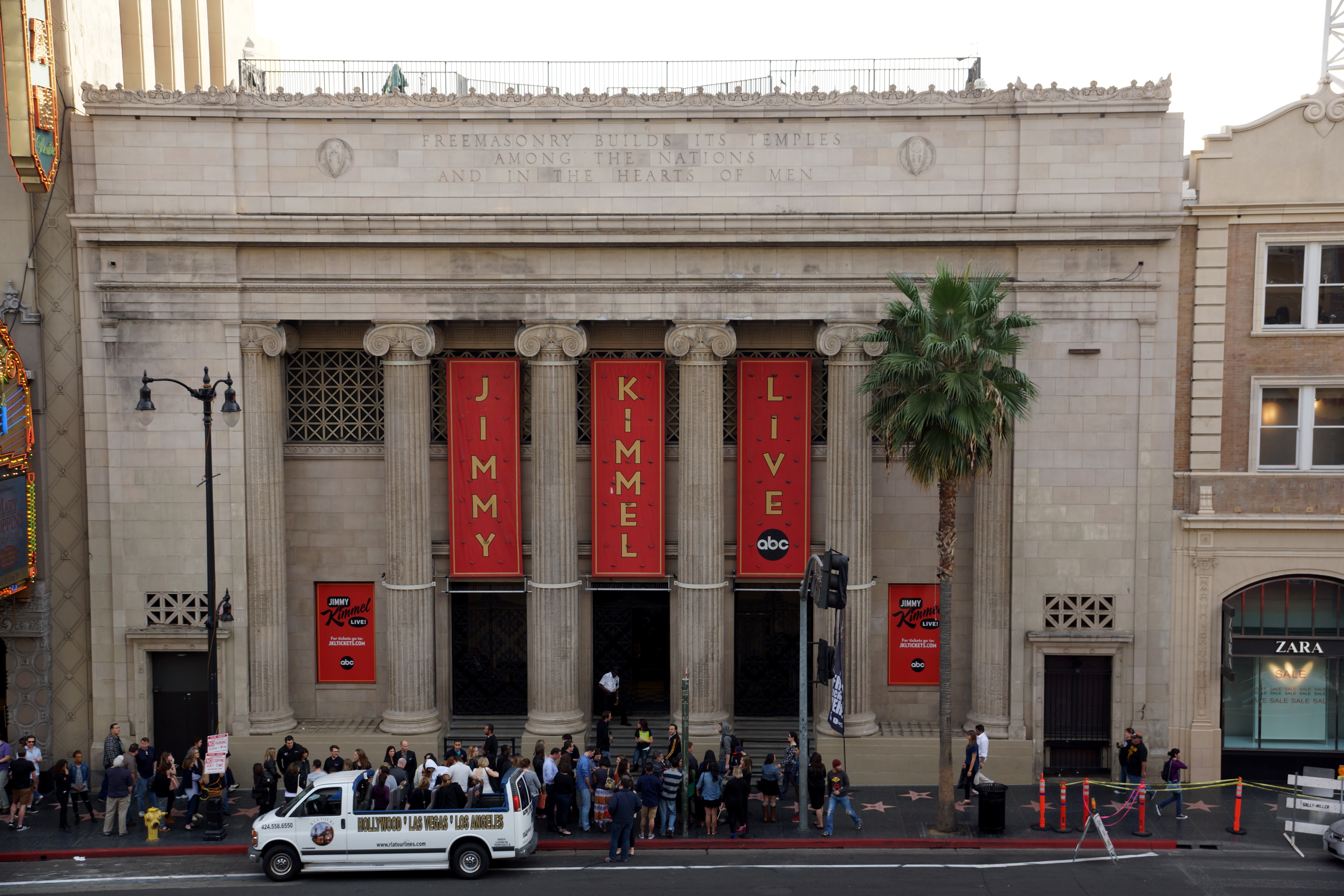 Exterior of the El Capitan Theatre with "Jimmy Kimmel Live" banners hanging between columns, and a crowd gathered outside