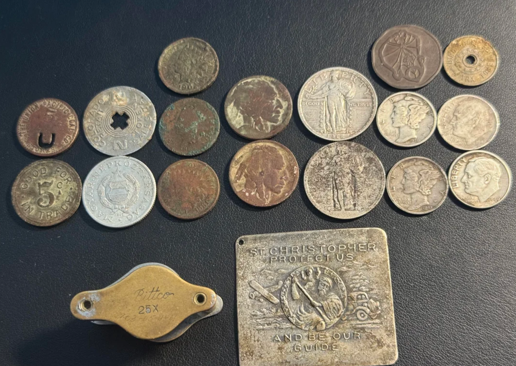 Samling av vintage mynter, et lommeuringshus og en metall St. Christopher -medaljon på en mørk overflate