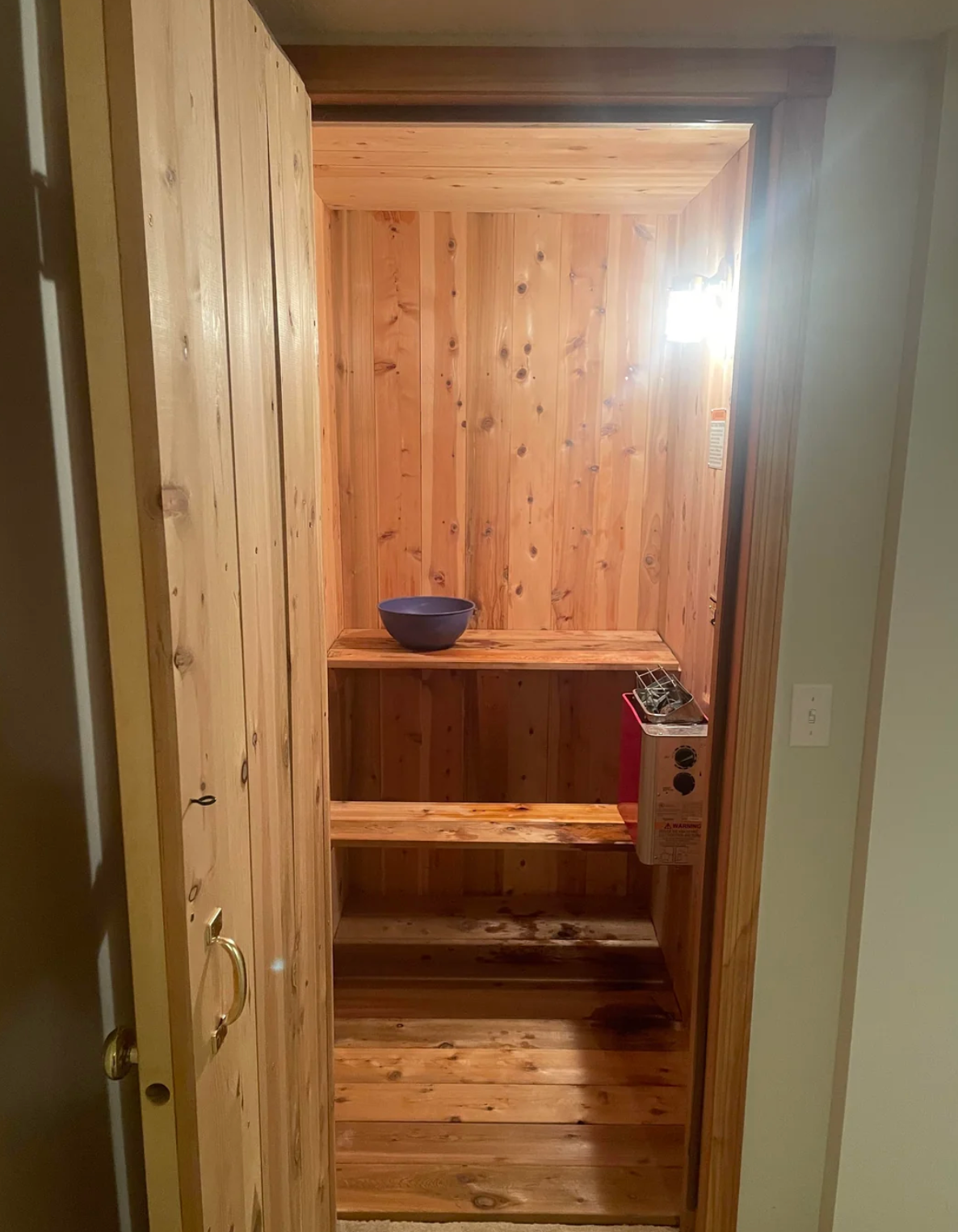 Liten badstue med en blå bolle på en hylle inni. Døren er åpen, og et lys lyser inn interiøret