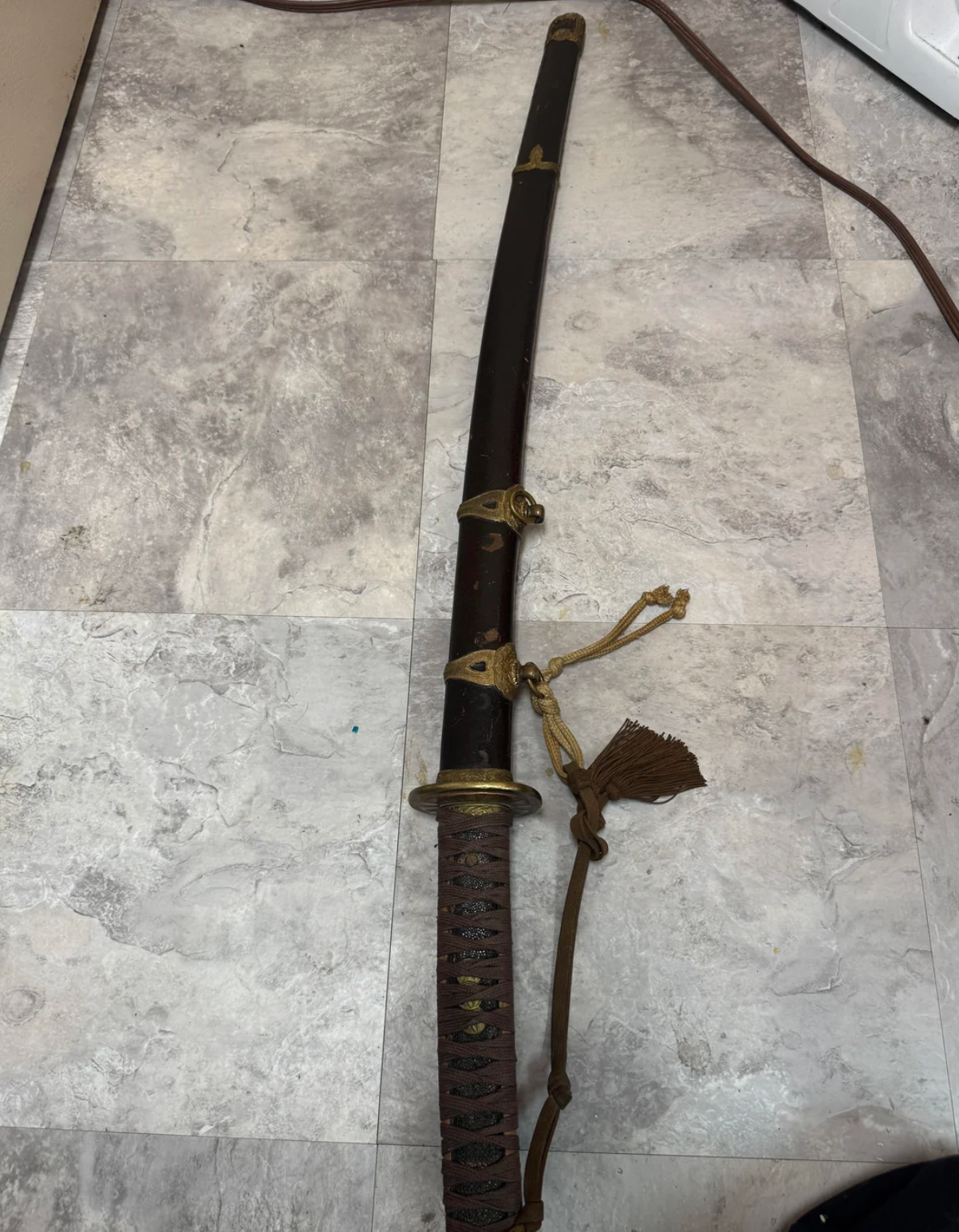 En tradisjonell katana med et utsmykket håndtak og skjede ligger på et flislagt gulv