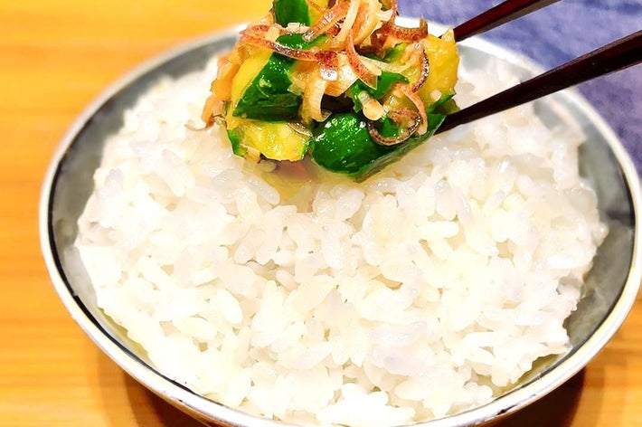 白いご飯の上に、箸で持ち上げられた野菜と薬味のトッピングがあります。