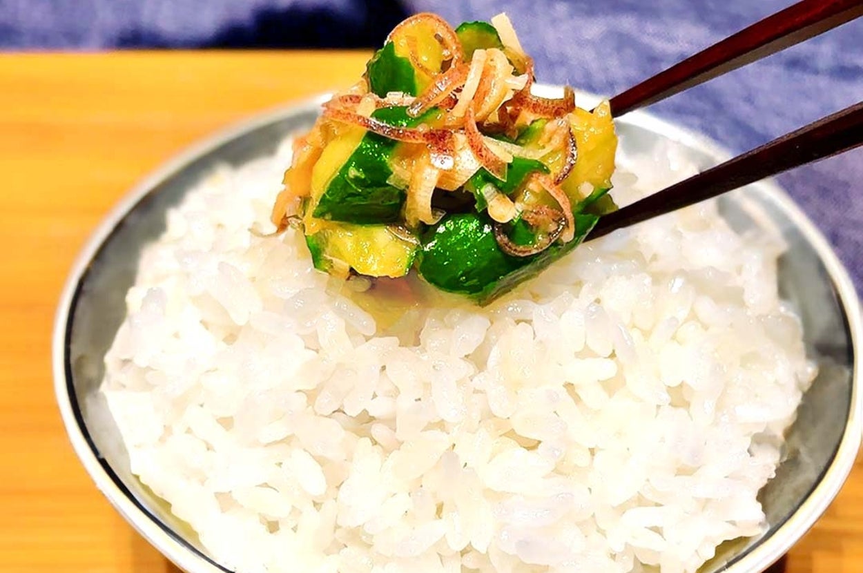 白いご飯の上に、箸で持ち上げられた野菜と薬味のトッピングがあります。