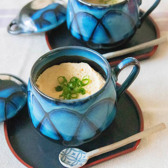青い陶器カップに入った茶わん蒸しが2つ、ネギがのっている。カップ横に小さなスプーンが添えられている。