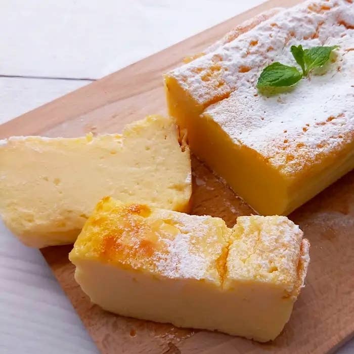 木製ボード上のスライスされたベイクドヨーグルトケーキ。ミントの葉がトッピングされています。