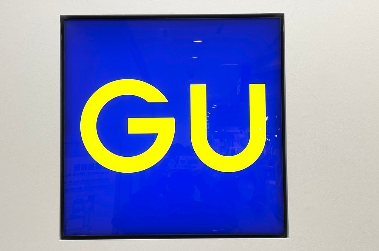 The image shows a square sign with large "GU" letters on it