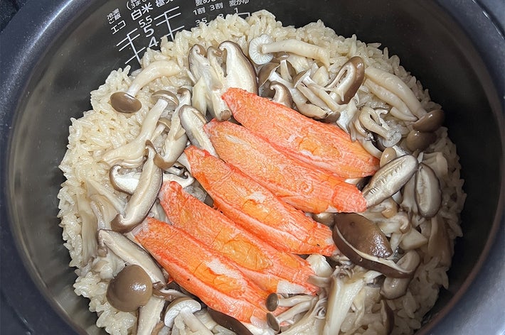 炊飯器で炊かれた鮭ときのこの炊き込みご飯。鮭が中央に並べられ、きのこが周囲に配置されています。