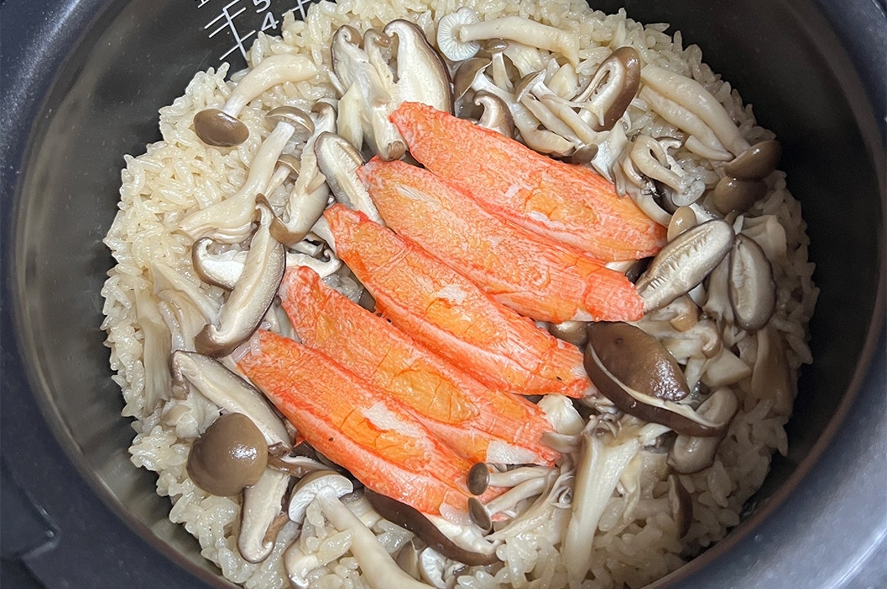 炊飯器で炊かれた鮭ときのこの炊き込みご飯。鮭が中央に並べられ、きのこが周囲に配置されています。