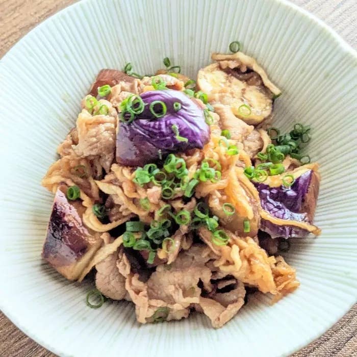 切り干し大根と豚肉のポン酢炒め。器に盛られた豚肉となすの炒め物。上には刻んだネギがトッピングされている。