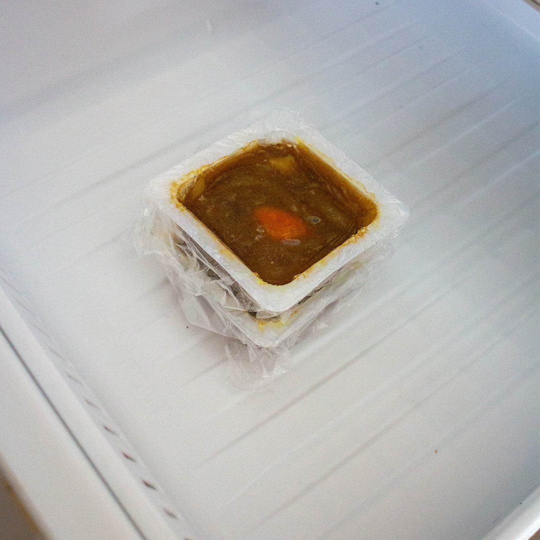 冷蔵庫の中に小さな容器に入った食べ物。ラップで覆われています。