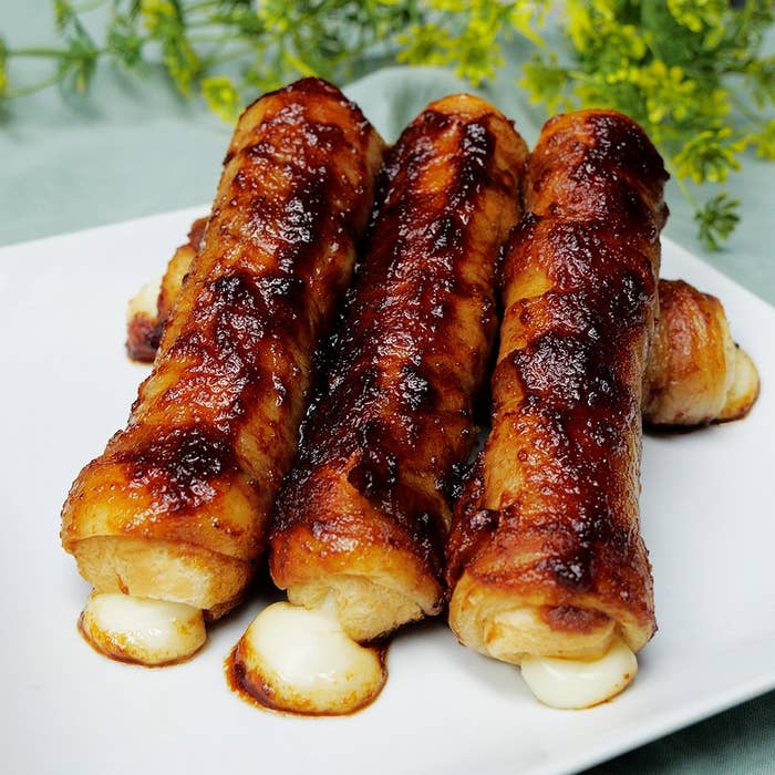 お皿に載ったチーズ入りのベーコン巻き、食欲をそそる見た目。背景に植物が見える。
