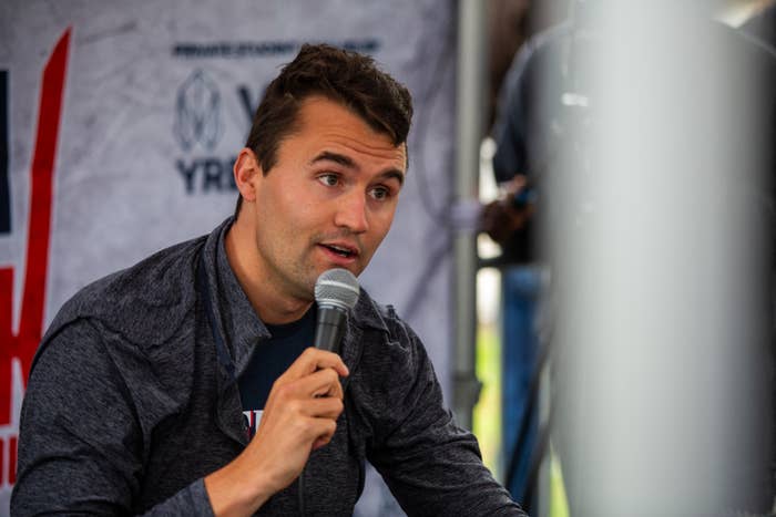 A idiosyncratic speaking into a microphone astatine an event, sitting against a backdrop with disposable logos and text