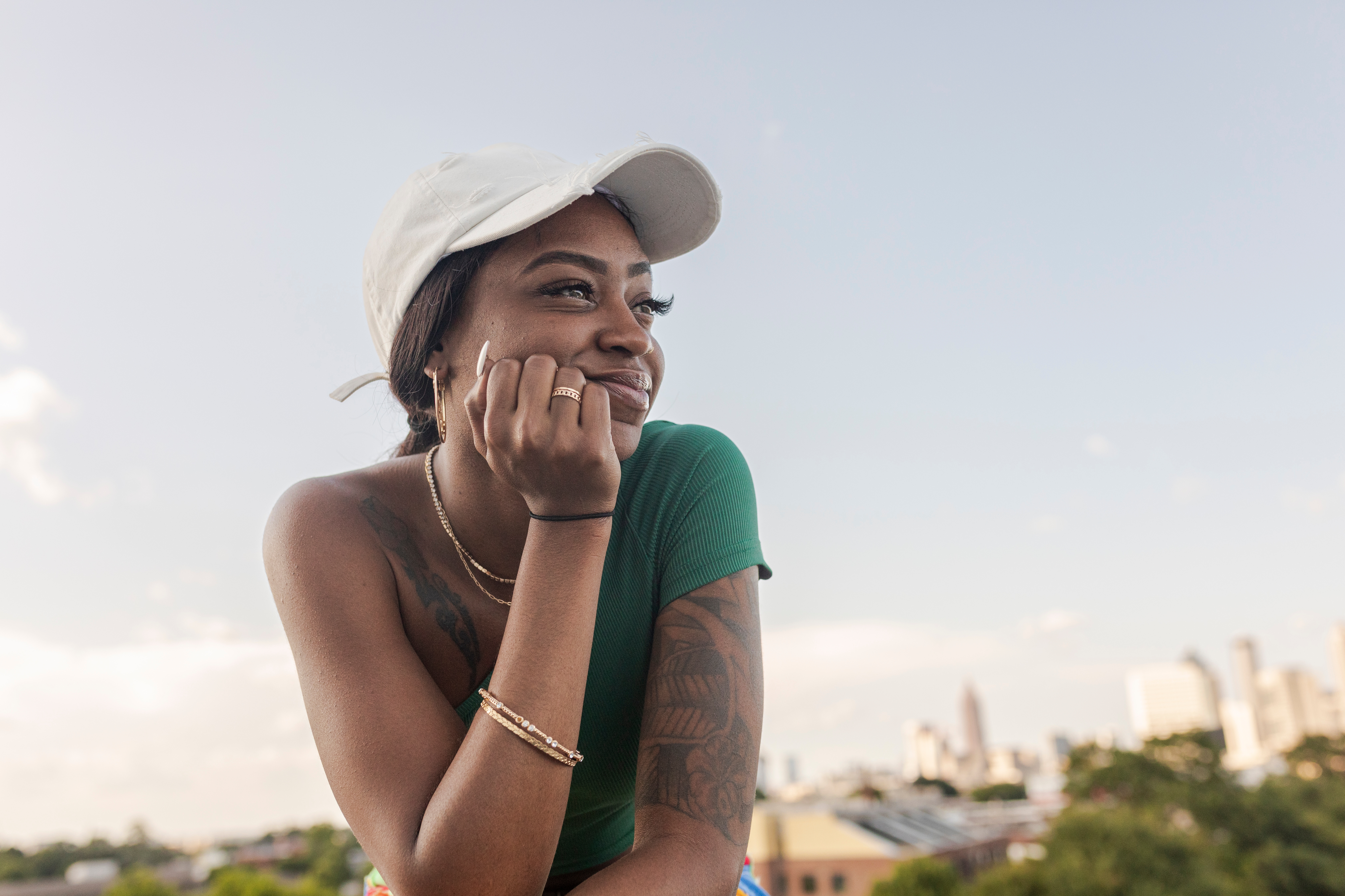 Person utendørs, iført en baseballhette og uformell antrekk, smilende mens du ser på avstanden, med en byens skyline i bakgrunnen