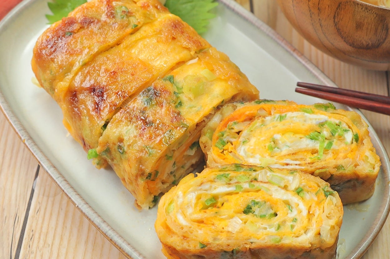 厚焼き玉子が皿に盛られ、味噌汁が添えられている朝食セット。玉子は緑の食材が巻き込まれている。