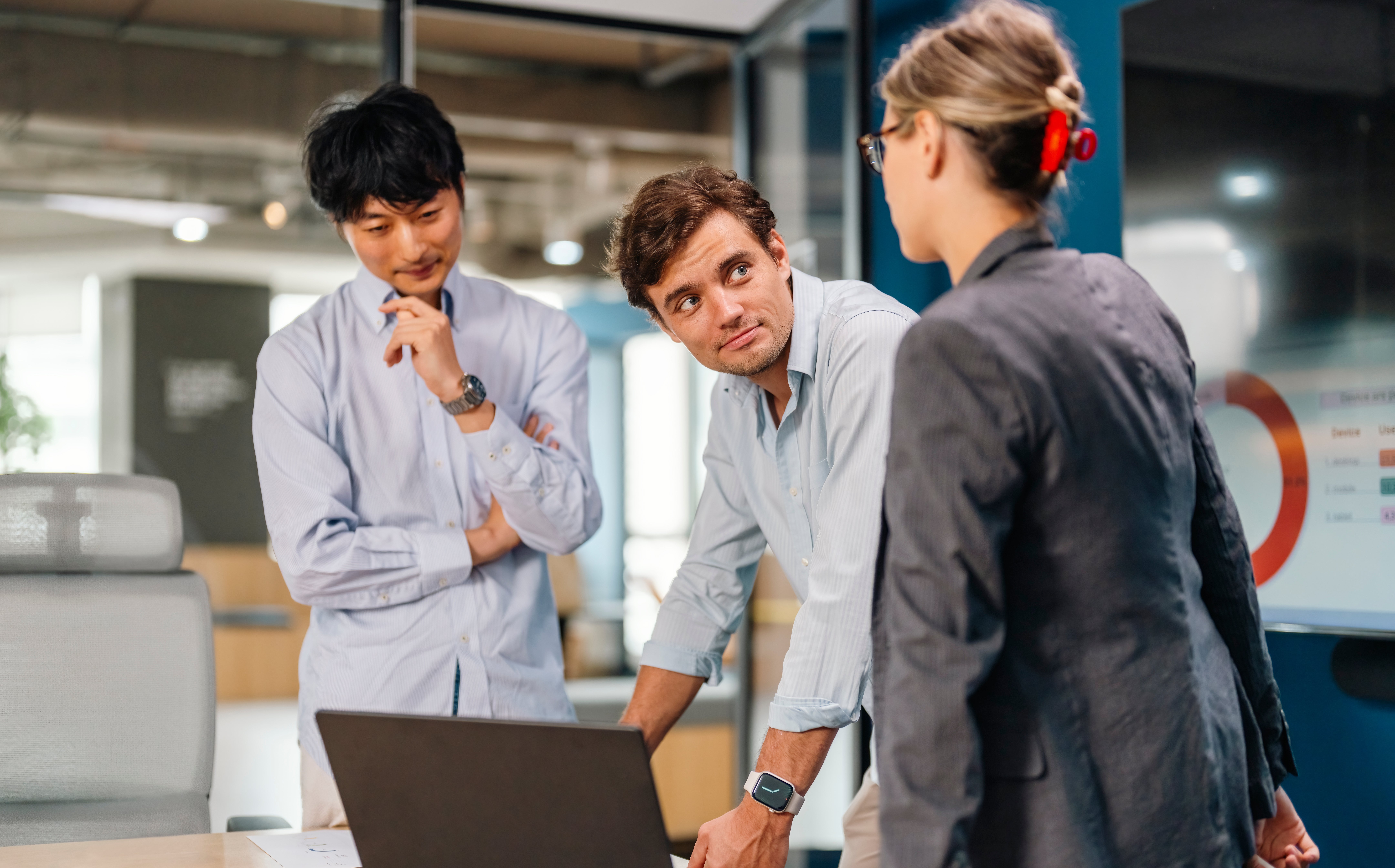 Tre fagpersoner i diskusjon rundt en bærbar PC, inne på et kontor. En kvinne har på seg en blazer; To menn er oppmerksomt engasjert