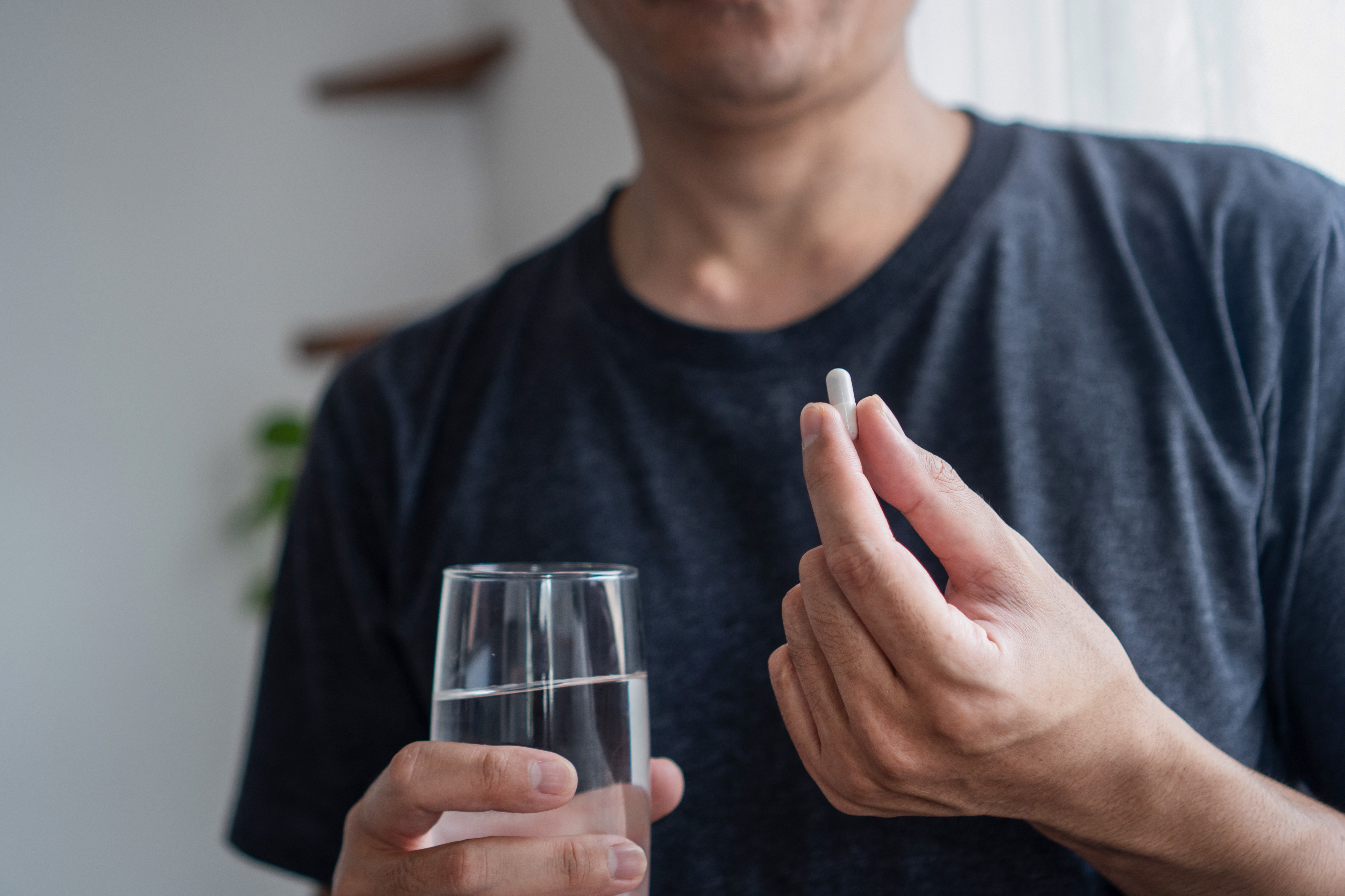 Person som holder en pille i den ene hånden og et glass vann i den andre, noe som tyder på medisiner eller tilleggsinntak