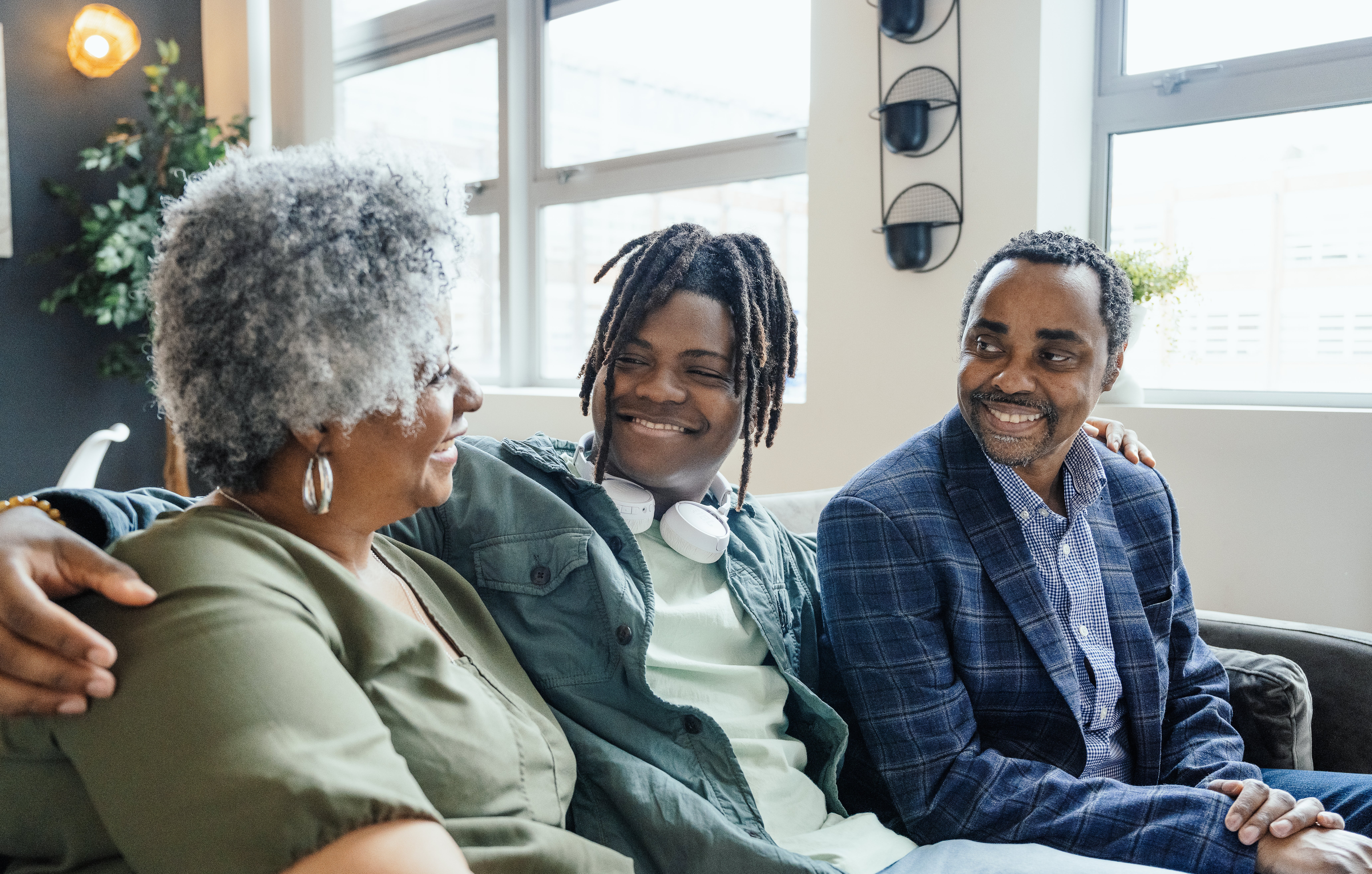 Tre personer som sitter på en sofa, smiler og snakker. Den ene har hodetelefoner rundt nakken. Innstillingen er uformell og vennlig