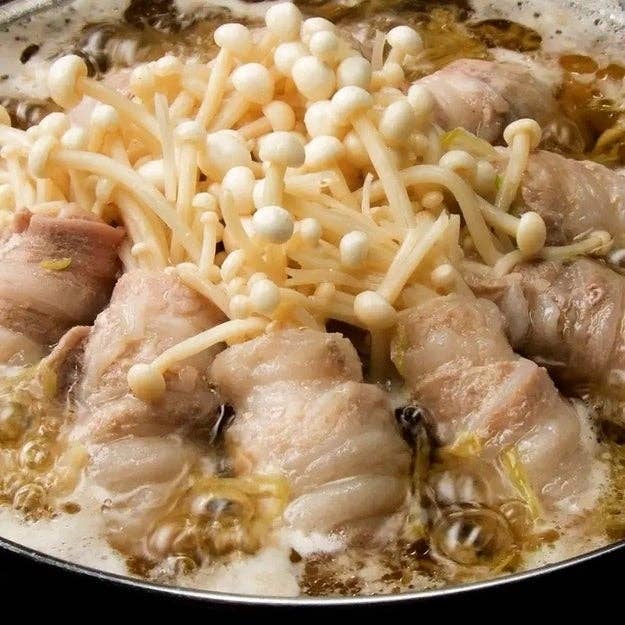 食材を煮込んでいる鍋。豚肉で巻かれたエノキ茸が中心に盛られている。
