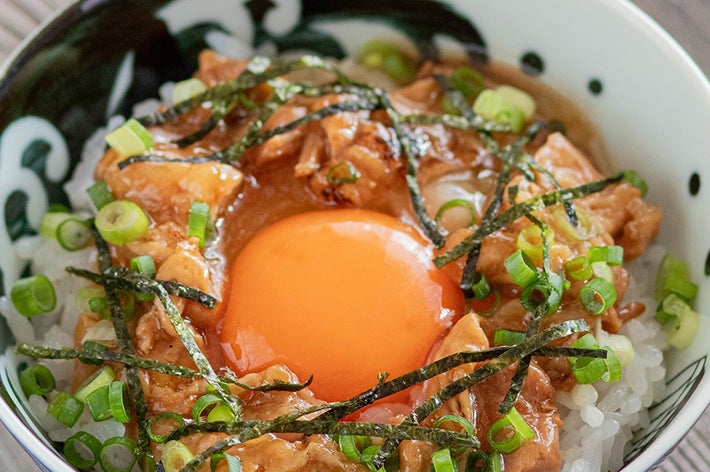 ご飯の上に生卵、刻んだネギ、海苔、味付け鶏肉が乗った丼ぶり。