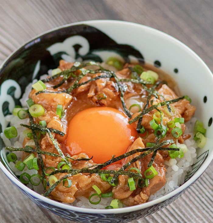 ご飯の上に生卵、刻んだネギ、海苔、味付け鶏肉が乗った丼ぶり。