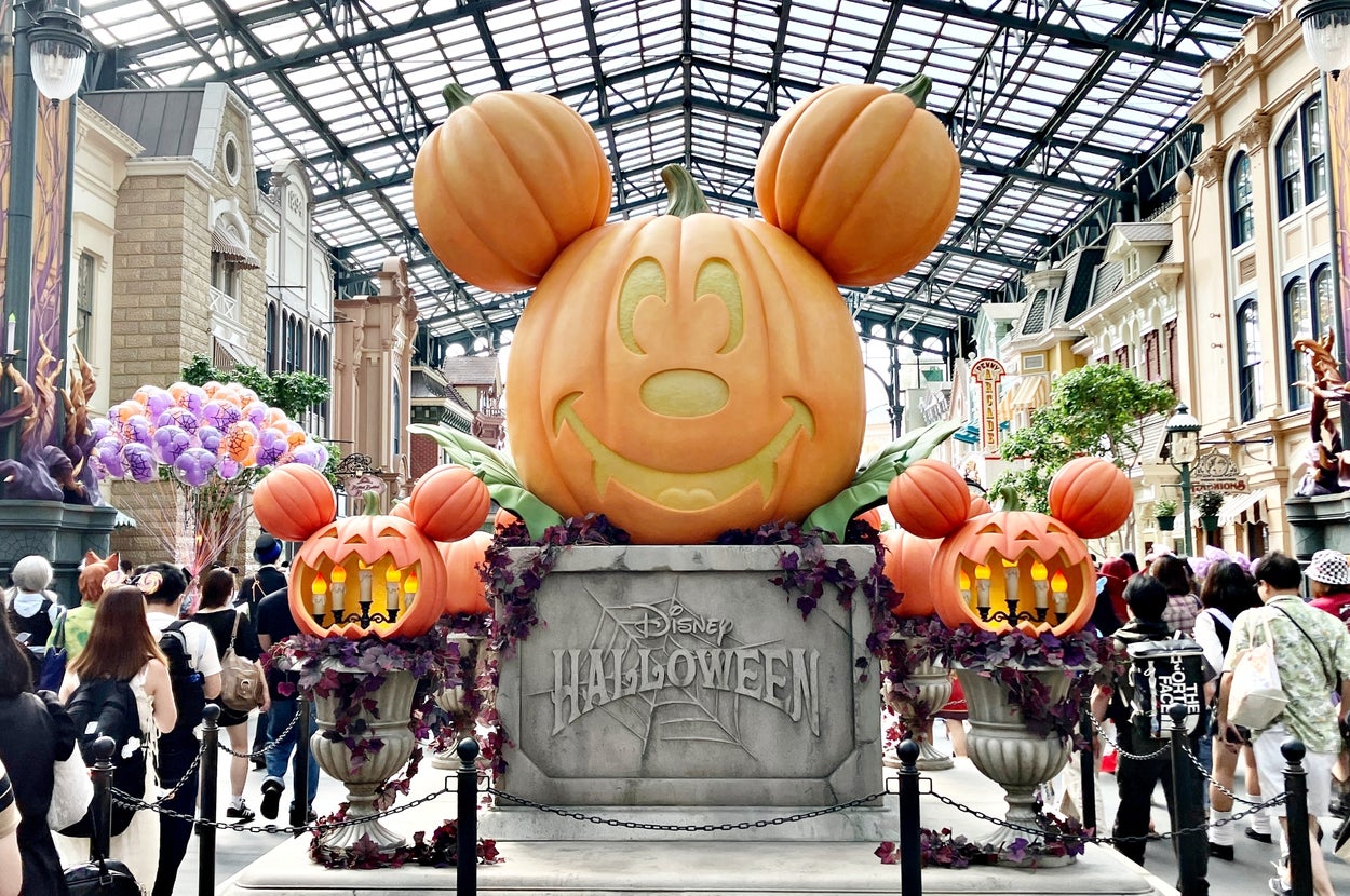 ディズニーのハロウィーンイベントで、ミッキーマウス型の大きなカボチャ装飾が飾られ、多くの来場者が訪れている。