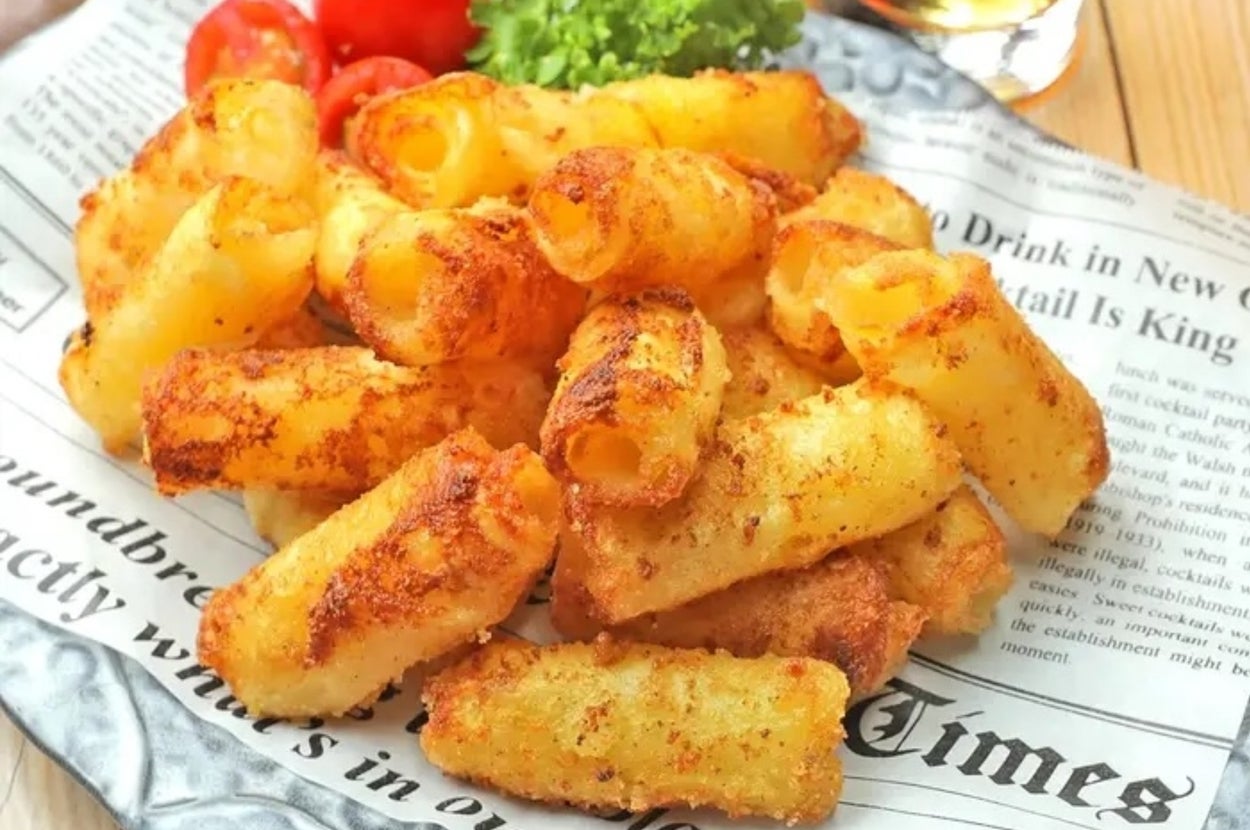 プレートに盛られた油で揚げたポテトスナック。背景にトマトとパセリ、新聞が敷かれている。