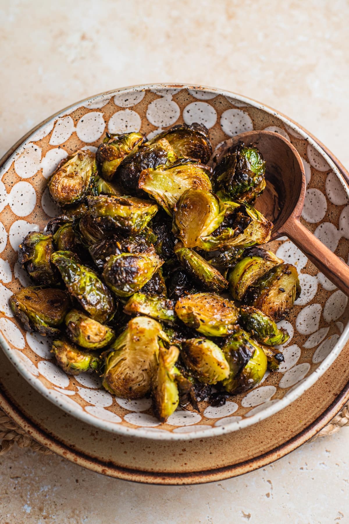 A bowl of roasted Brussels sprouts, slightly charred, on a rustic plate with a wooden spoon