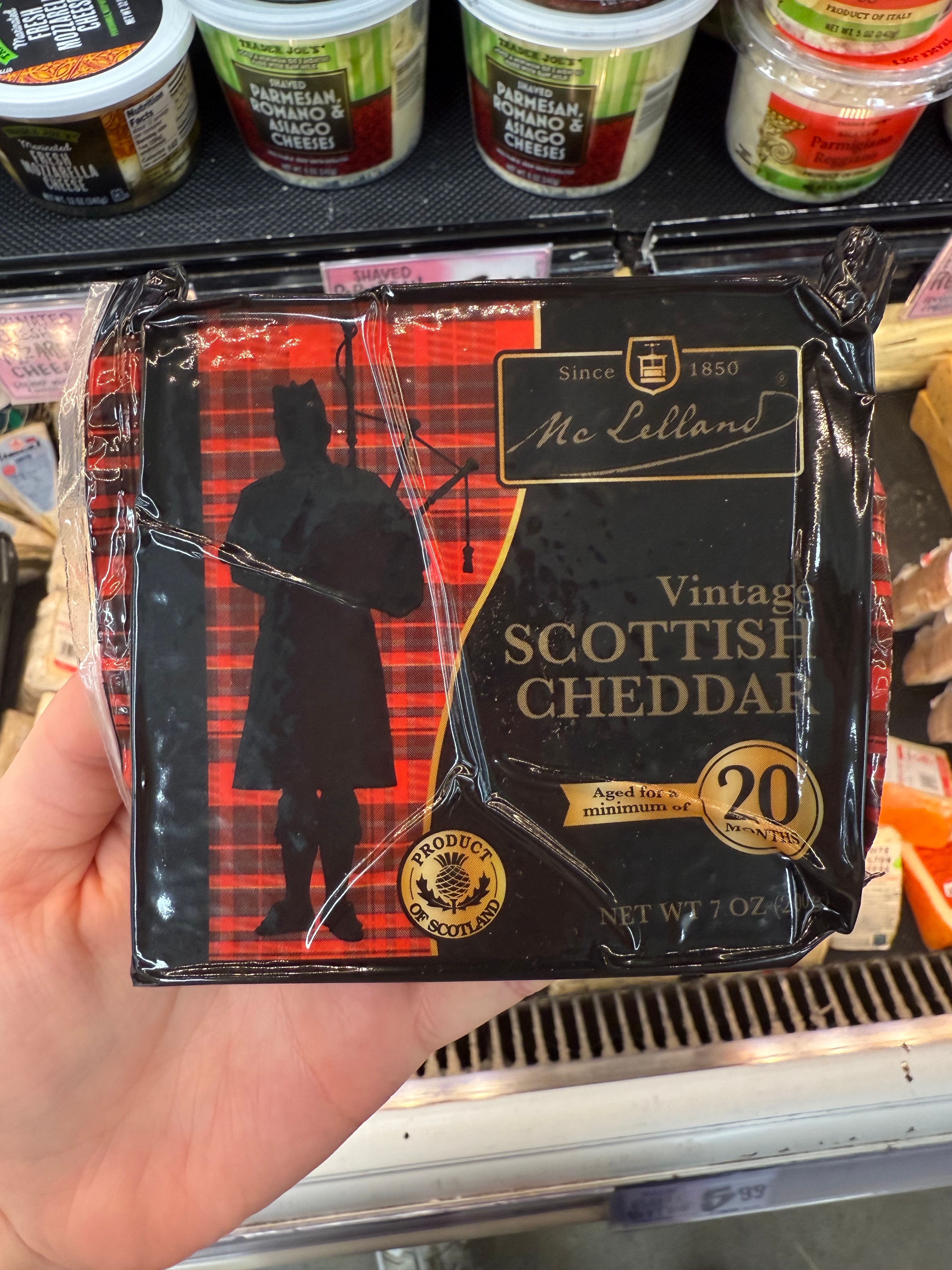 A block of vintage Scottish cheddar cheese, labeled as aged over 20 months, held in a store aisle