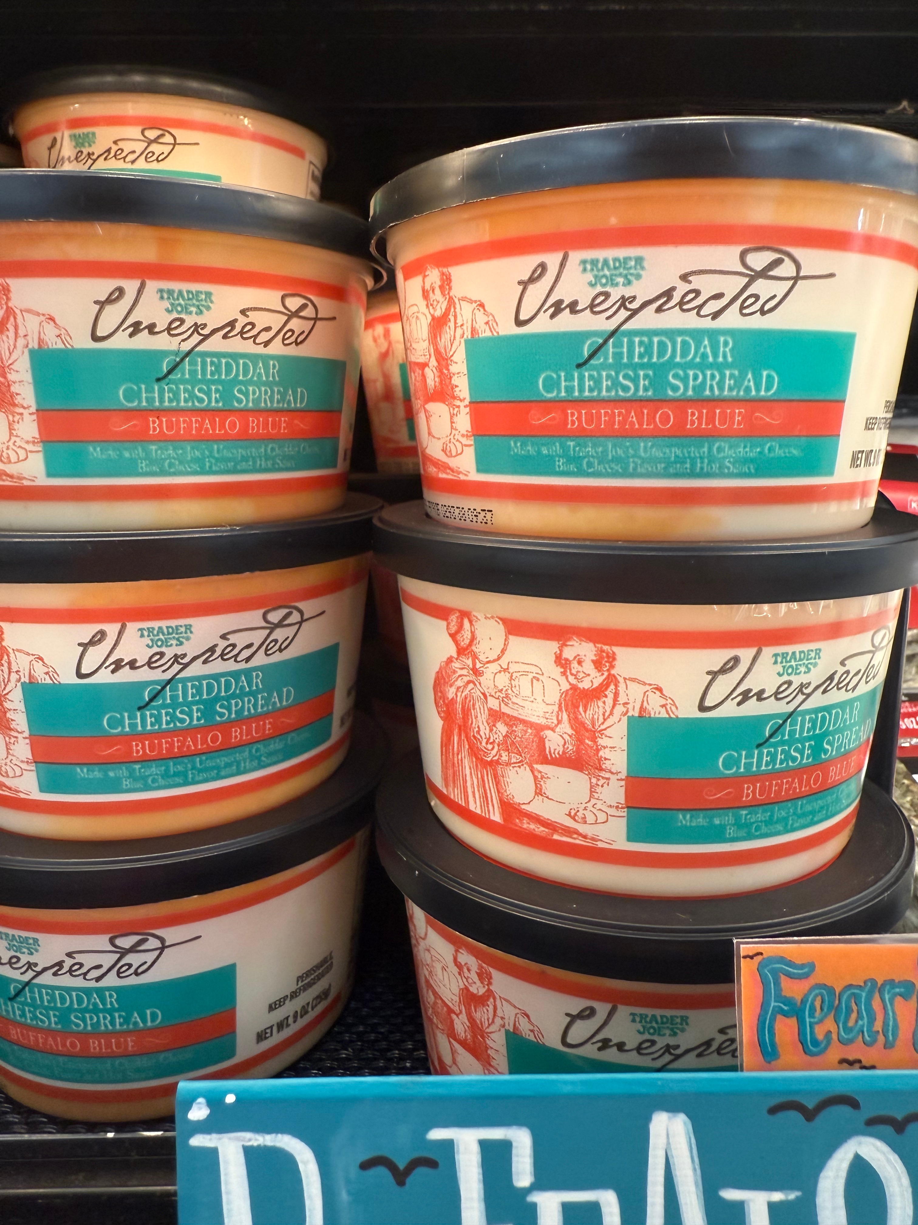 Containers of Trader Joe&#x27;s Unexpected Cheddar Cheese Spread with Buffalo Blue on a store shelf