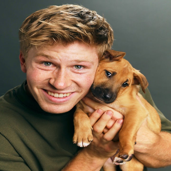 Person holding a puppy close to their face, both looking at the camera. The person is smiling broadly
