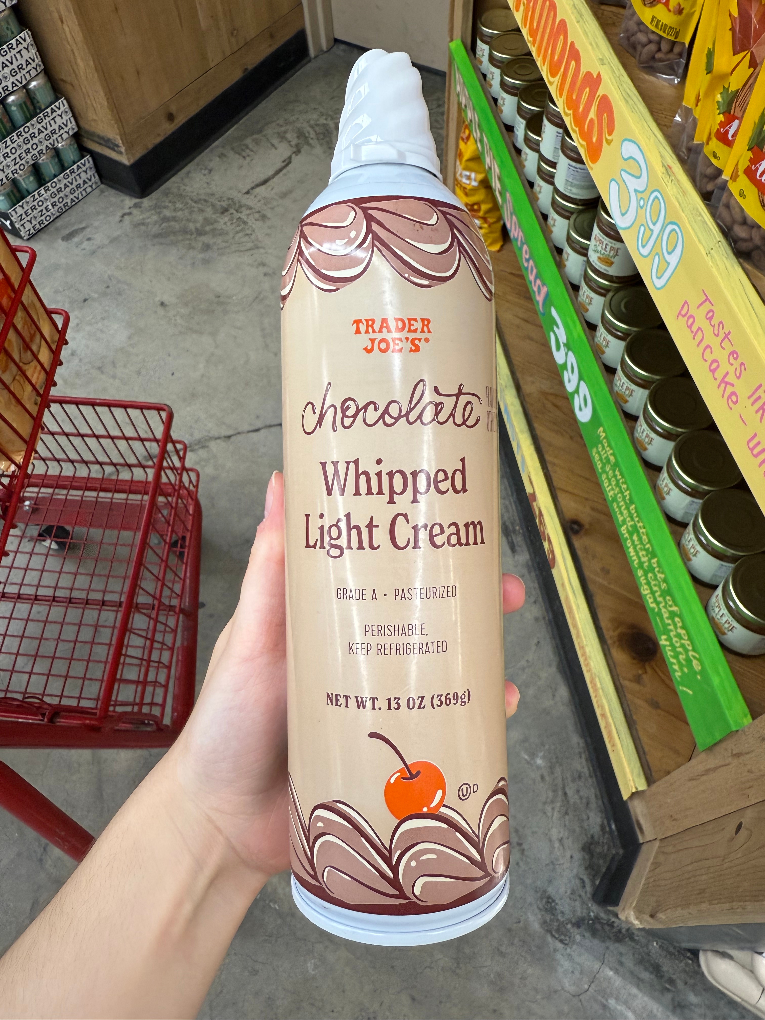A hand holding a can of Trader Joe's chocolate whipped light cream in a grocery store aisle