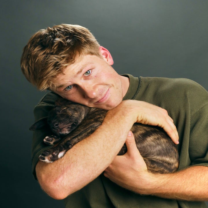 A person embraces a small brindle dog, smiling warmly at the camera