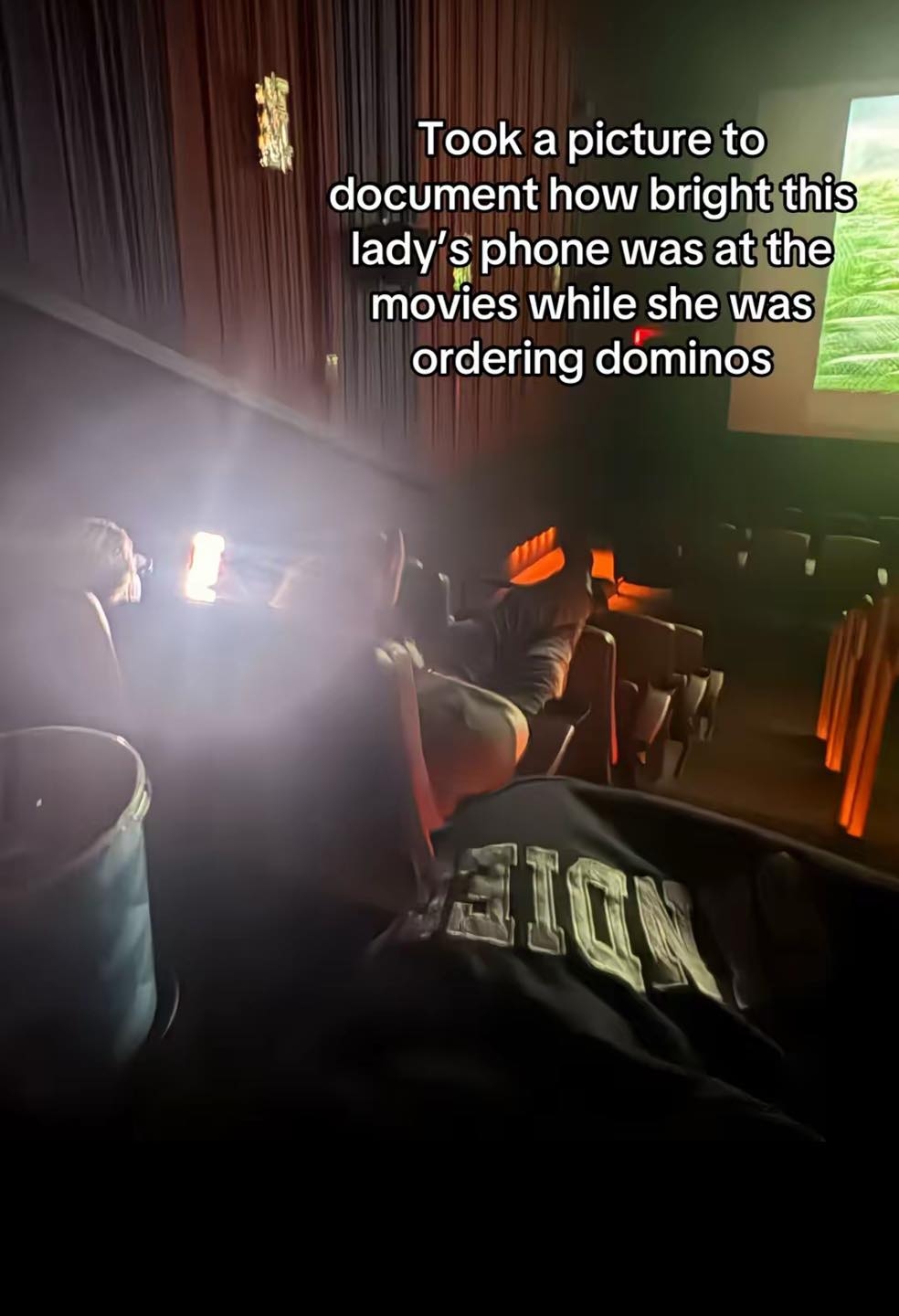 Person using a bright phone in a dark movie theater with text noting they are ordering food