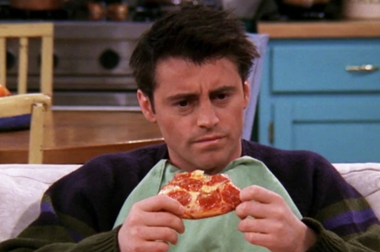 Person with a concerned expression sits on a couch holding a slice of pizza
