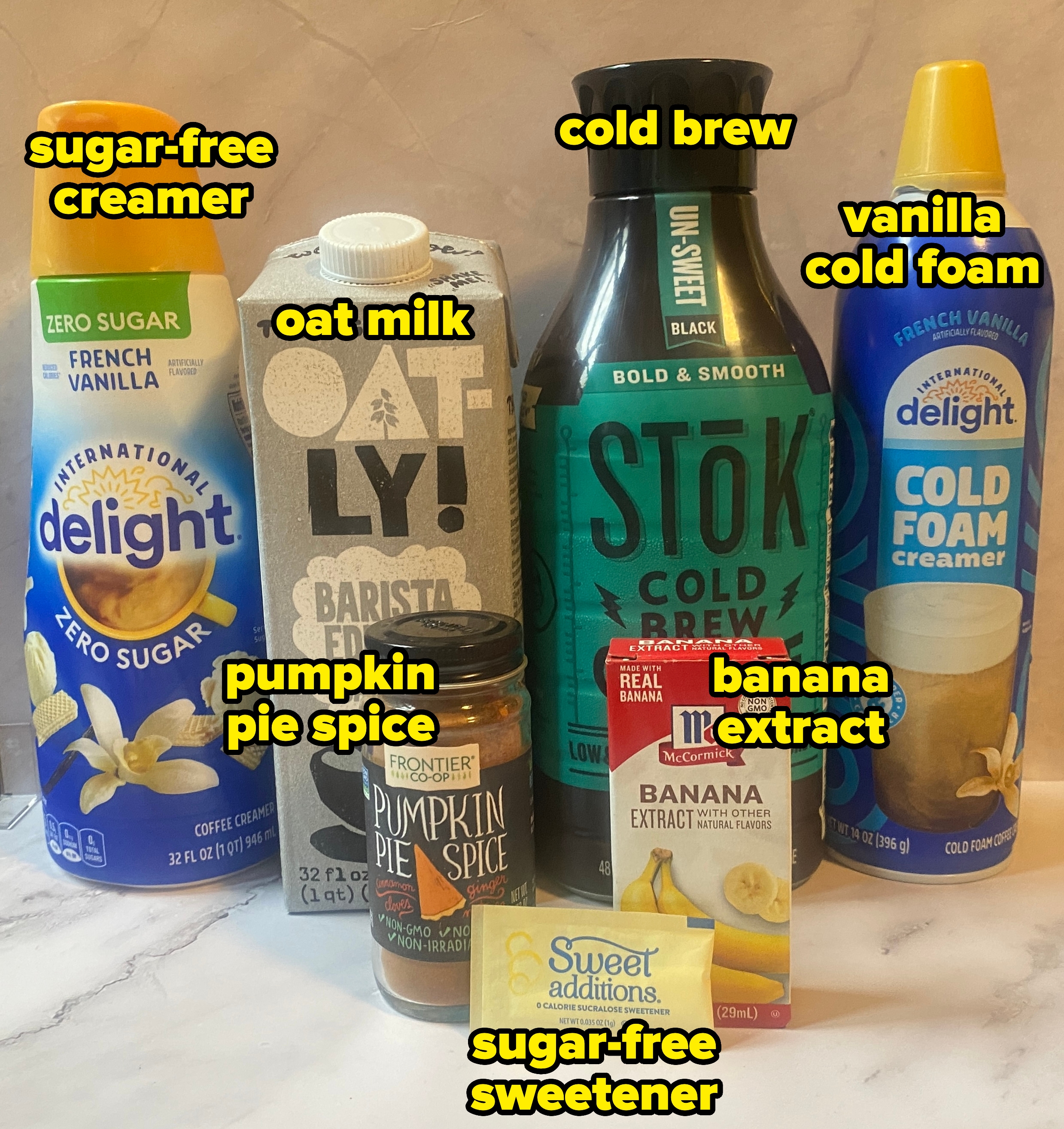 Various coffee products, including creamers, cold brew, pumpkin pie spice, vanilla extract, and sweetener, arranged on a marble surface
