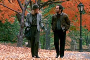 Sally and Harry from When Harry Met Sally walking in a park with fallen autumn leaves on their path, colorful trees all around them