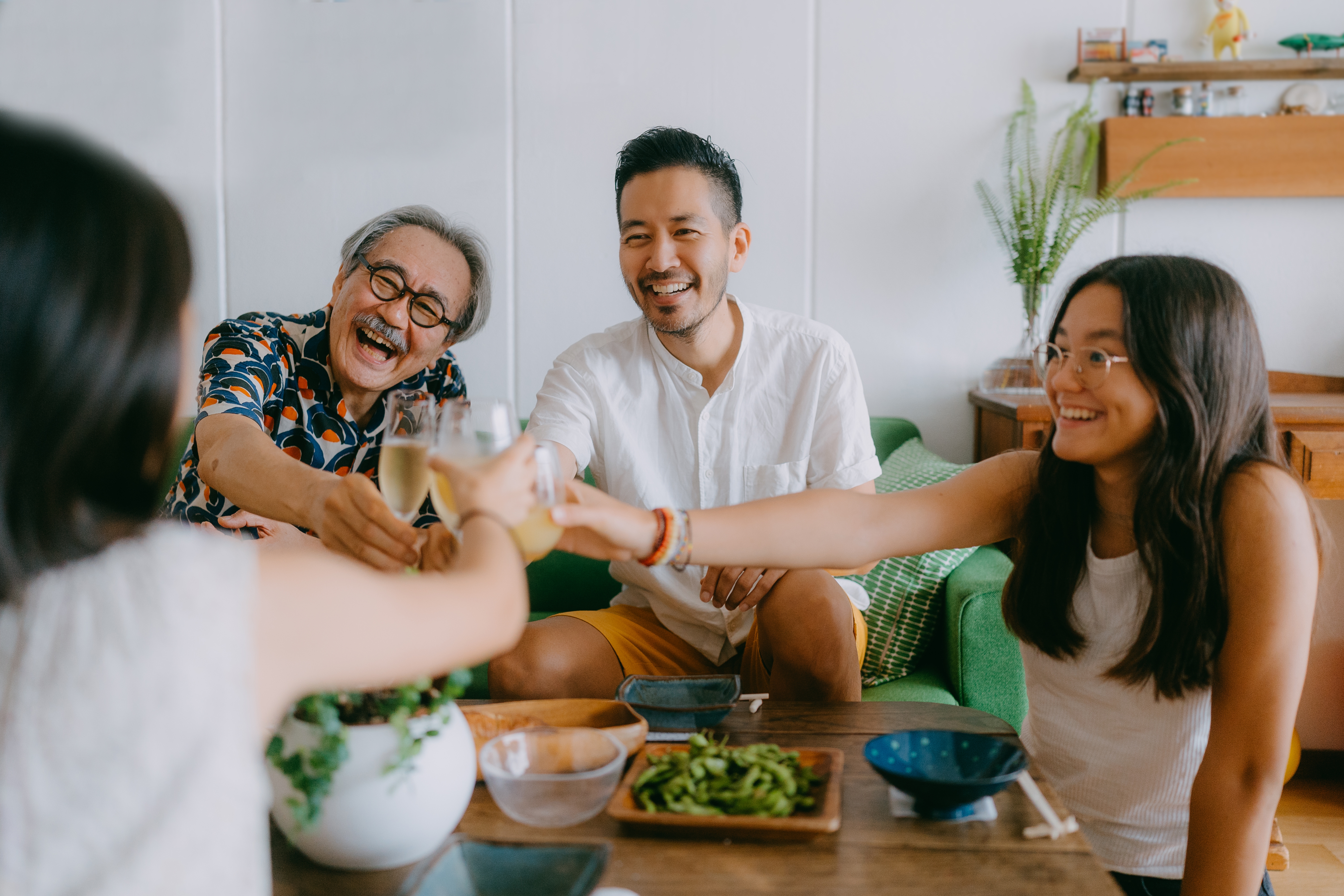 Familie og venner rister gledelig briller rundt et spisebord, og nyter en uformell samling med latter og samtale