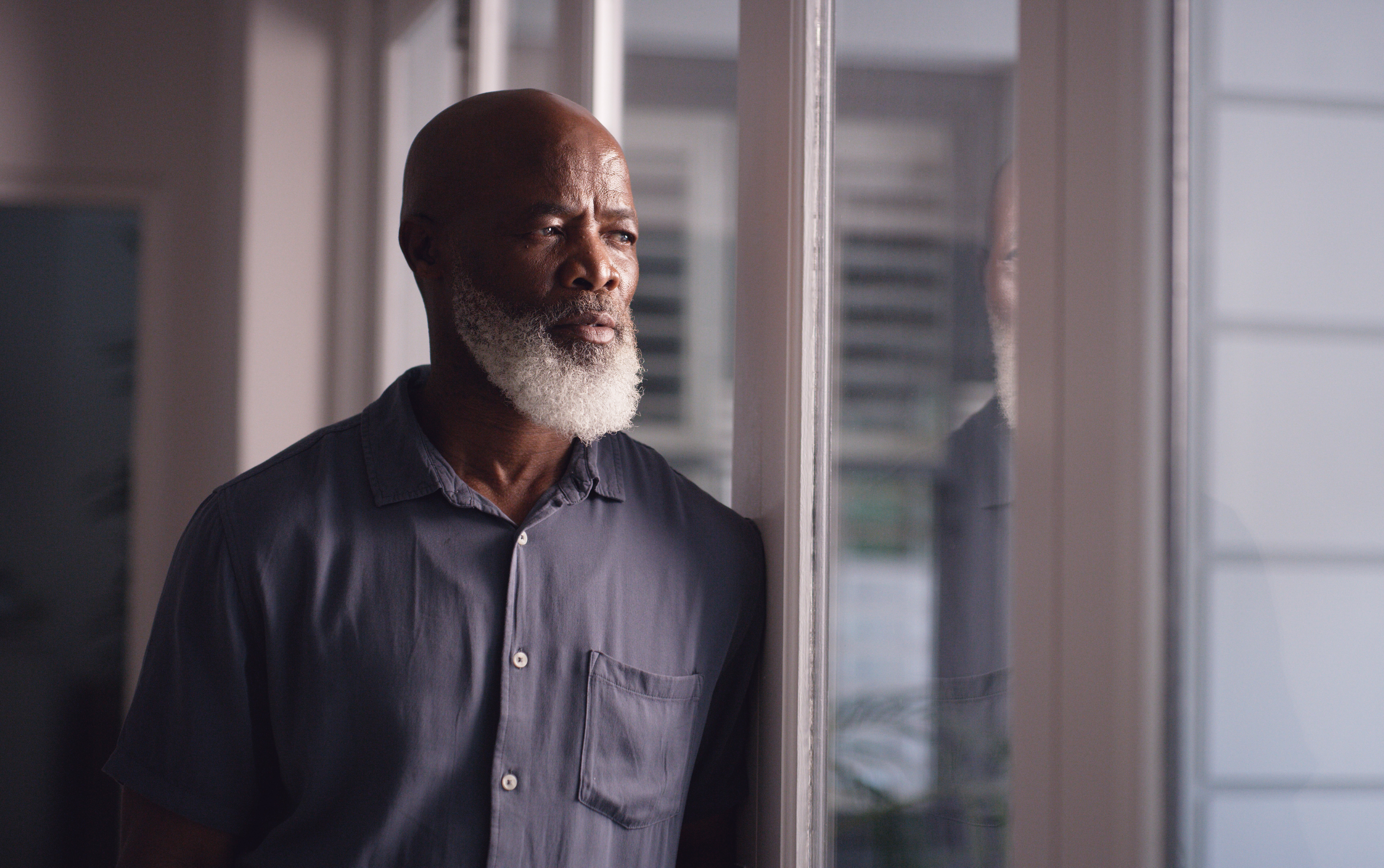 Eldre mann med hvitt skjegg iført en knapp-up-skjorte stirrer gjennomtenkt ut av et vindu