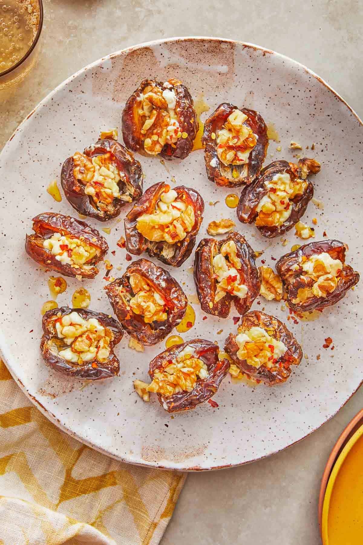 Plate of stuffed dates with nuts and cheese, drizzled with oil, on a speckled dish