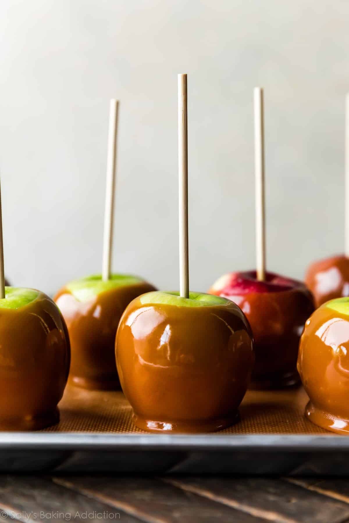 Caramel-dipped apples on a tray, each with a wooden stick, ready for serving