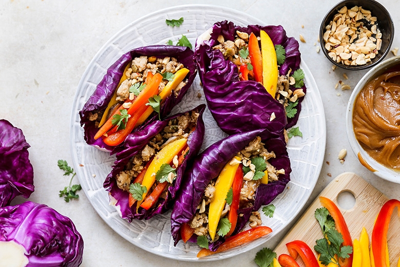 Plate of lettuce wraps filled with veggies, topped with nuts and cilantro, accompanied by dipping sauce and pepper slices