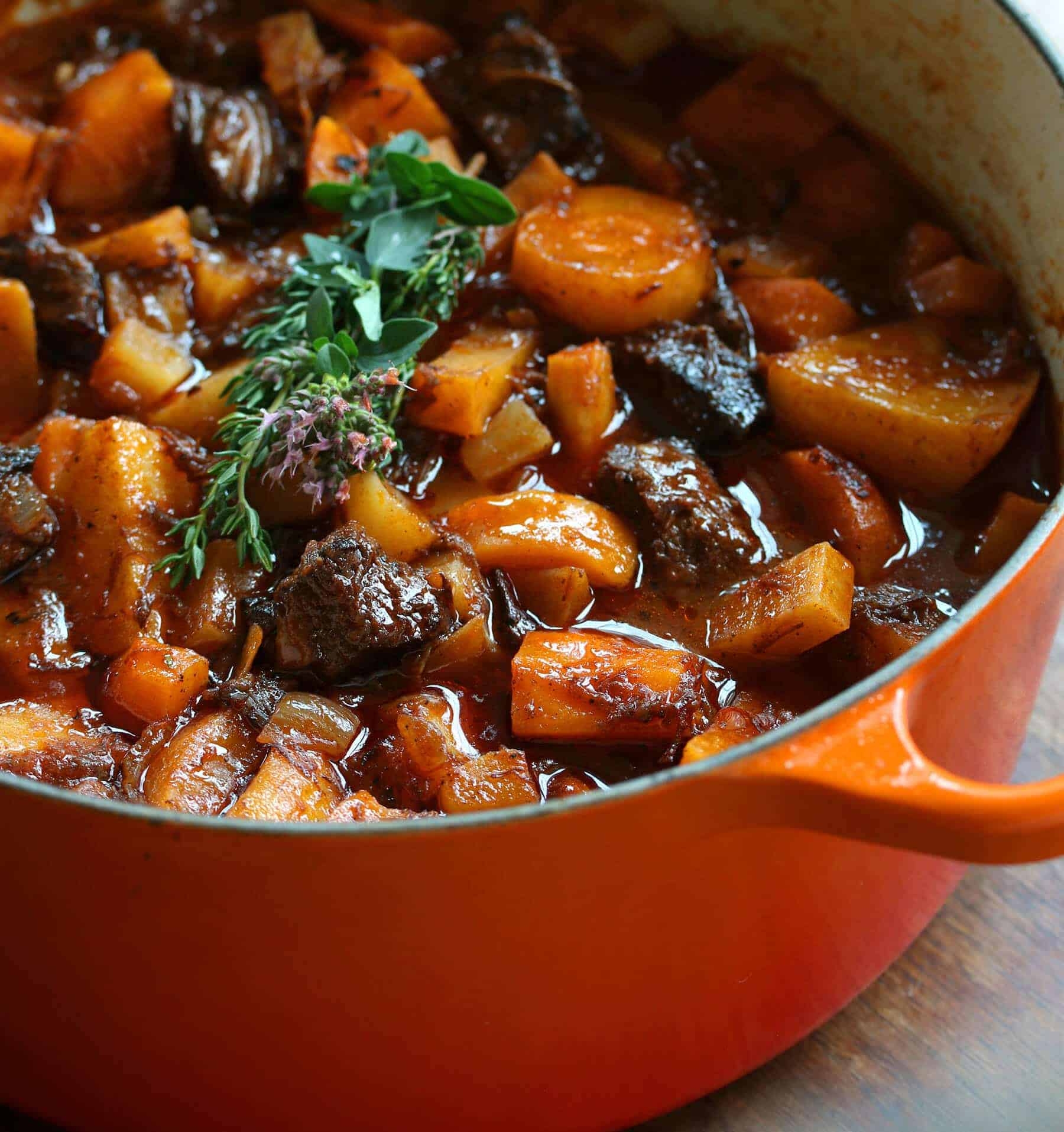 Hearty beef stew with chunks of meat, potatoes, and carrots in a pot, garnished with a sprig of fresh herbs