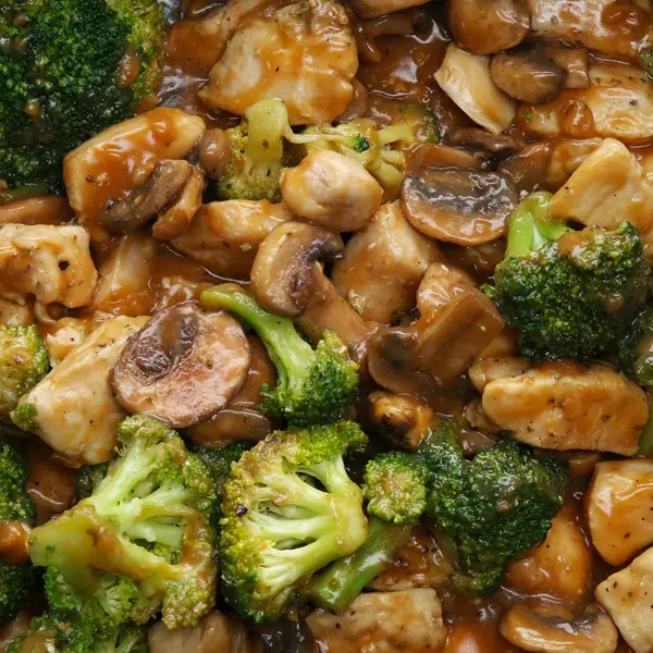 Close-up of a stir-fry dish featuring chunks of chicken, broccoli florets, and sliced mushrooms in a savory sauce