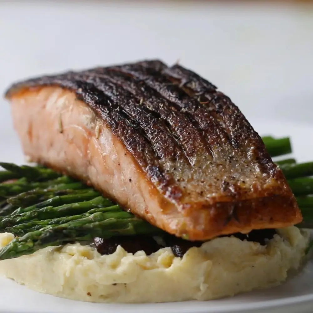Grilled salmon fillet atop cooked asparagus and mashed potatoes, plated elegantly for dining